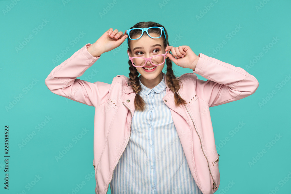 Happy funny girl in casual or hipster style, pigtail hairstyle, standing, holding two blue and pink glasses and looking away with toothy smile, Indoor studio shot, isolated on blue or green background Happy funny girl in casual or hipster style, pigtail hairstyle, standing, holding two blue and pink glasses and looking away with toothy smile, Indoor studio shot, isolated on blue or green background