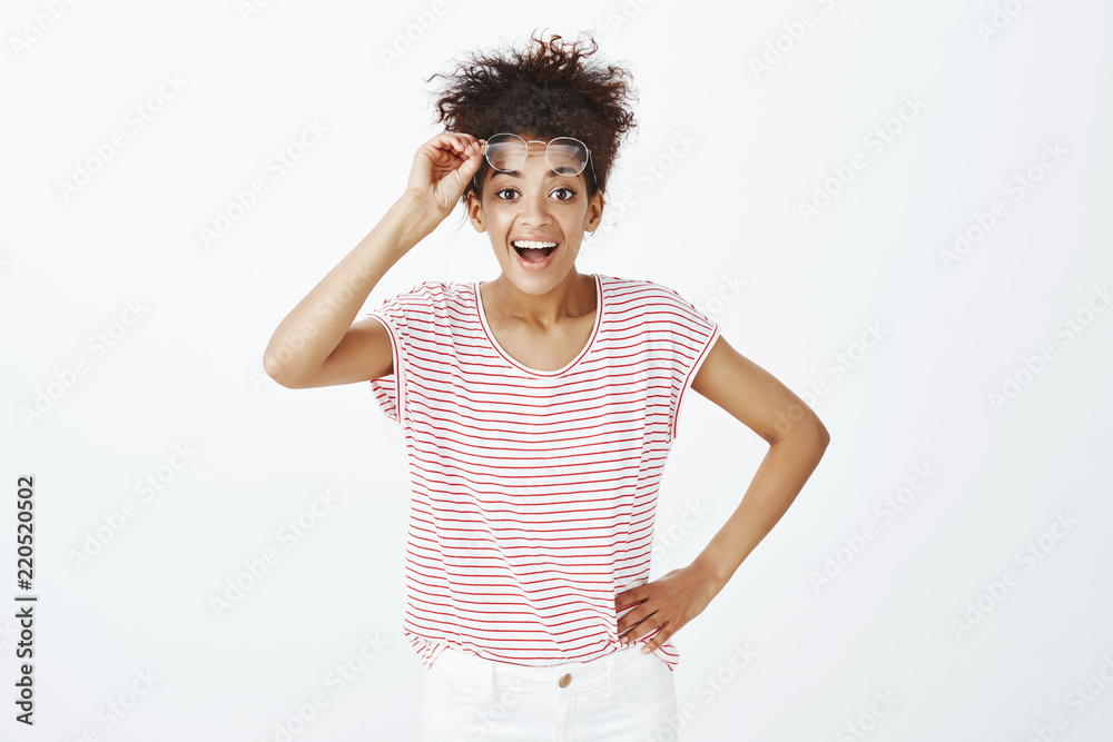 Portrait of pleased friendly woman with curly combed hair, holding hand on hip, taking off glasses and smiling broadly, seeing familiar face in foreign country, meeting friend and having bad sight Portrait of pleased friendly woman with curly combed hair, holding hand on hip, taking off glasses and smiling broadly, seeing familiar face in foreign country, meeting friend and having bad sight