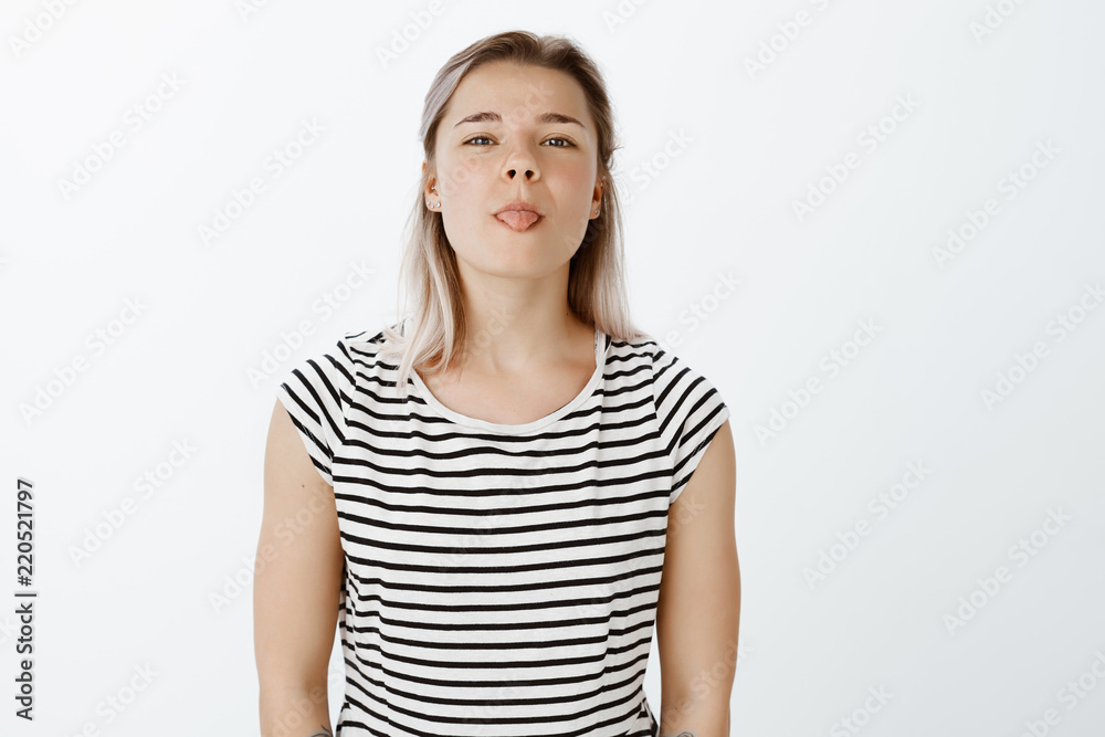 Indoor shot of playful good-looking woman in striped t-shirt, tilting head and showing tongue, being childish and in great mood, playing with friend and making faces while being bored during classes Indoor shot of playful good-looking woman in striped t-shirt, tilting head and showing tongue, being childish and in great mood, playing with friend and making faces while being bored during classes
