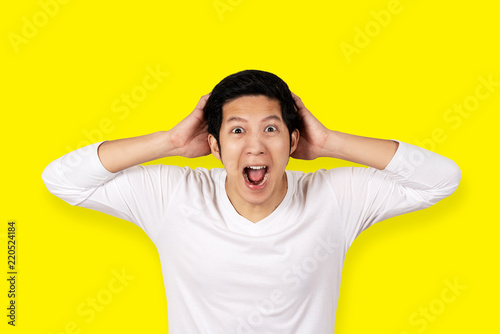 Young attractive asian man in casual white shirt looking at camera with feeling amazed, excited or shocked face with open mouth on isolated yellow background. Funny face expression concept.