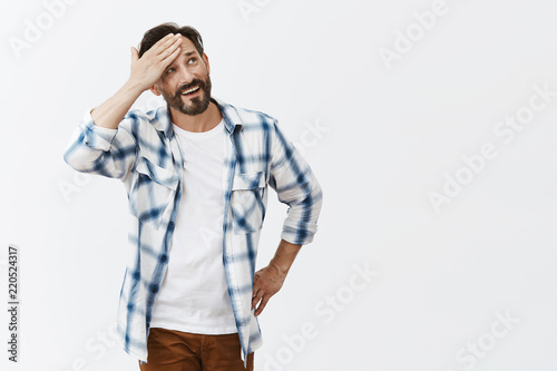 Phew, almost got in trouble. Portrait of relieved good-looking happy male breathing air out and whiping sweat from forehead while smiling broadly and gazing up, walking under hot sun over grey wall