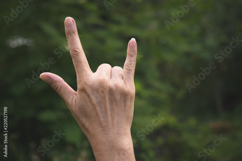 Closeup hand of person doing symbol for i love you in garden green nature background. © mintra