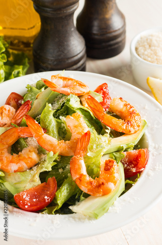 Fresh Caesar shrimp salad with delicious prawns  ruccola  spinach  cabbage  arugula  egg  parmesan and cherry tomato on wooden background. Oil  salt and pepper. Healthy and diet food concept.
