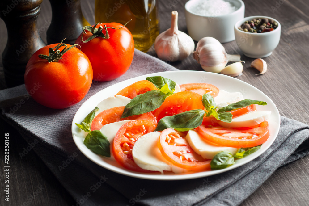 Photo of Caprese Salad with tomatoes, basil, mozzarella, olives and olive oil on wooden background. Italian traditional caprese salad ingredients. Mediterranean, organic and natural food concept. Photo of Caprese Salad with tomatoes, basil, mozzarella, olives and olive oil on wooden background. Italian traditional caprese salad ingredients. Mediterranean, organic and natural food concept.
