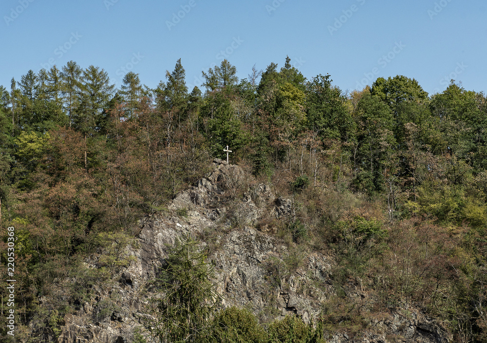 a wooden cross high on a rock protruding between autumn trees a wooden cross high on a rock protruding between autumn trees