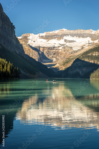 Fototapeta Naklejka Na Ścianę i Meble -  Amazing lake surrounded by mountains and glaciers, tourists doing kayak in a blue sky day in Banff National Park in Canada