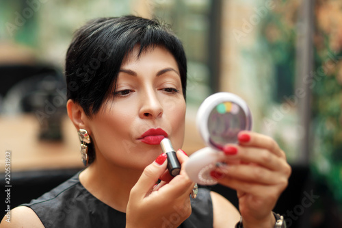 stylish brunette short-cut woman paints lips on the street looking in the mirror