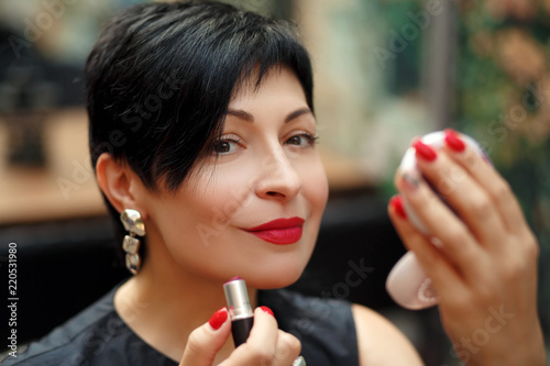 stylish brunette short-cut woman paints lips on the street looking in the mirror