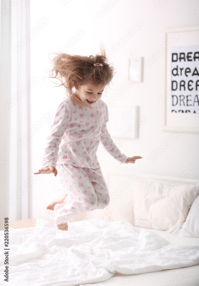 Cute little girl jumping on bed with soft pillows at home Cute little girl jumping on bed with soft pillows at home