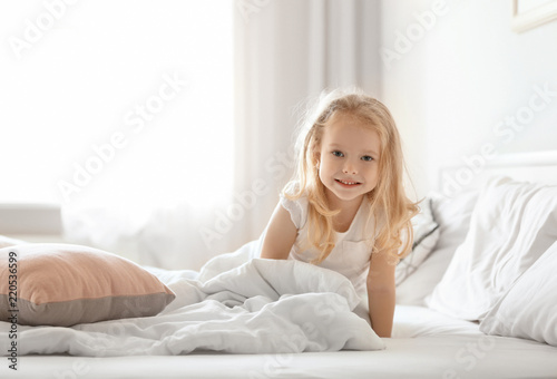 Cute little girl on bed with soft pillows at home © Africa Studio