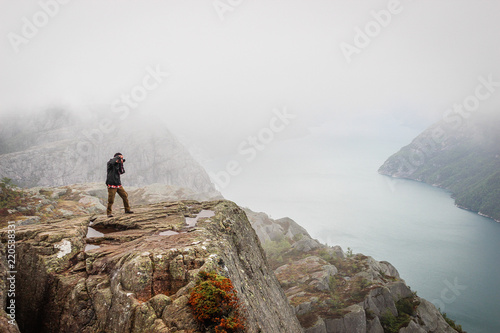 Nature photographer tourist with camera shoots while standing on the mountain. Norway Preikestolen or Prekestolen.