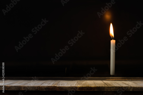 Wooden table in front of light candle burning brightly in the black background, can used for display or montage your products.