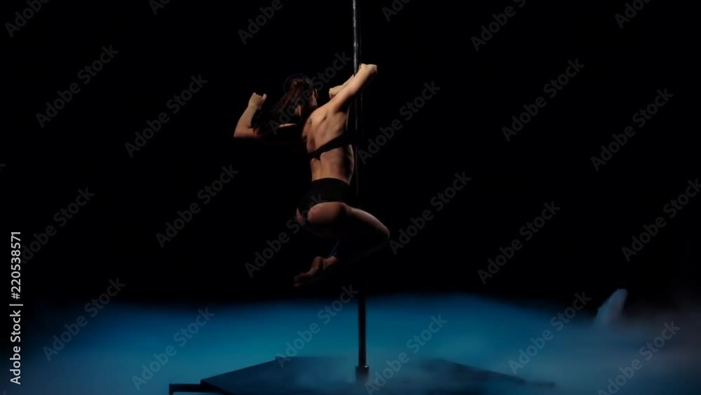 Striptease dancer in blue smoke on a pole. Black smoke background. Slow motion