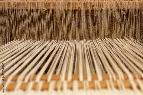 A close view of the brown threads of a warp of a loom going through the brown dents of the reed.