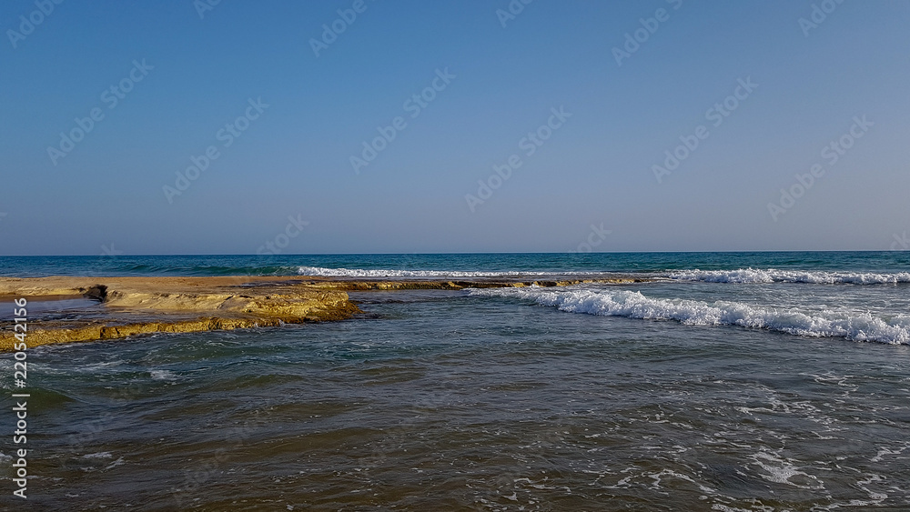 A rocky beach with sea waves and a clear sky on a sunny day. A rocky beach with sea waves and a clear sky on a sunny day.