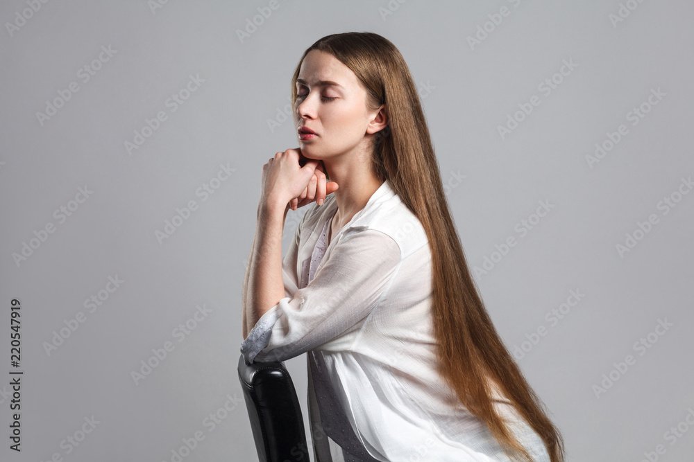 side profile view of calm beautiful young model actor with long brown hair in white t-shirt sitting with closed eyes and touching her chin with serious face. studio shot isolated on white background. side profile view of calm beautiful young model actor with long brown hair in white t-shirt sitting with closed eyes and touching her chin with serious face. studio shot isolated on white background.