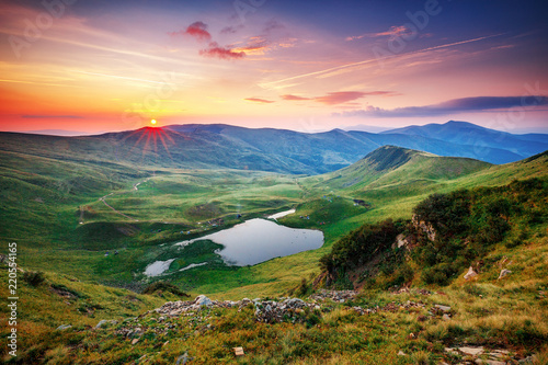 Breathtaking sunrise landscape - the lake Dogyaska in high mountains of Svydovets mountain chain system. Green, yellow and lilac colors in nature. Fantastic valley lit with morning sun, terrific view