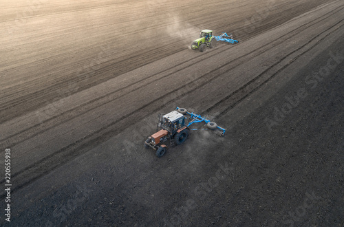 Aerial view of two blue tractors plows the earth in field on a summer day against a black earth background. Agriculture. Two tractors travel one after another along the black field © LALSSTOCK