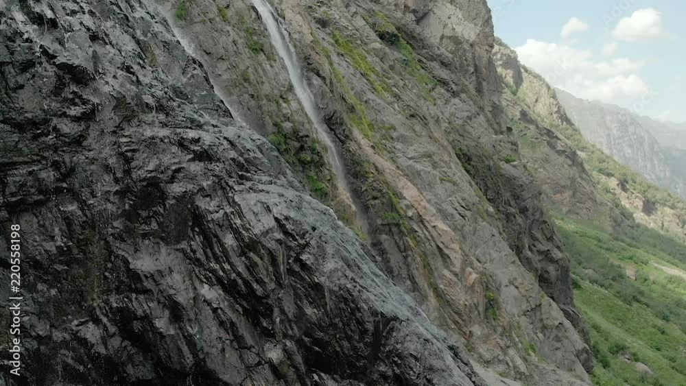 Tracking and top shot Air shot from a stream of water splashing waterfall on a rock wall in the Caucasus Mountains. Around the jet of the waterfall Tracking and top shot Air shot from a stream of water splashing waterfall on a rock wall in the Caucasus Mountains. Around the jet of the waterfall