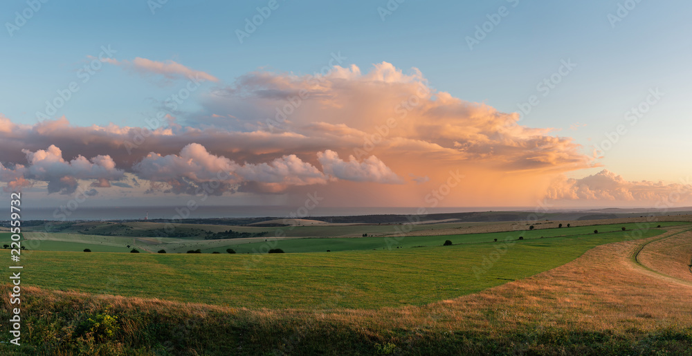 Stunning large panorama of Summer sunset landscape image of South Downs National Park in English countryside with stunning dramatic storm clouds out at sea in the distance