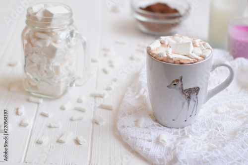 White cup with hot cocoa and marshmallow on the white wooden background