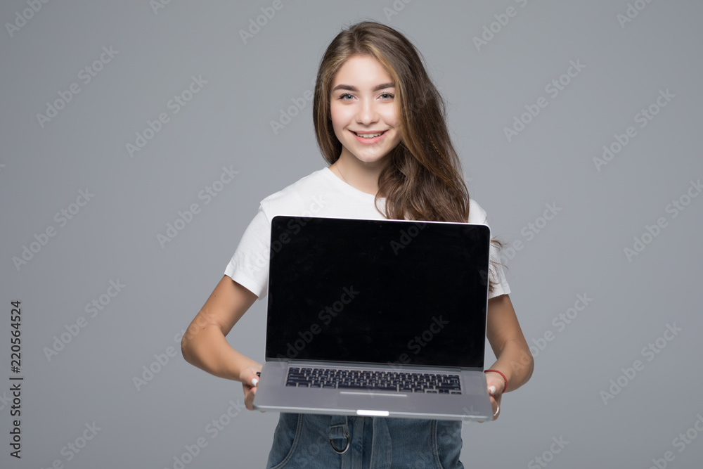 Naklejka premium Happy woman showing blank laptop screen over gray background.