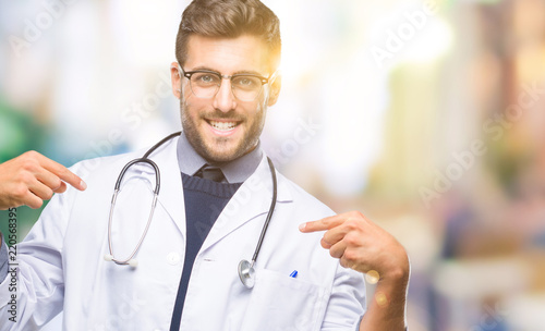 Young handsome doctor man over isolated background looking confident with smile on face, pointing oneself with fingers proud and happy. © Krakenimages.com