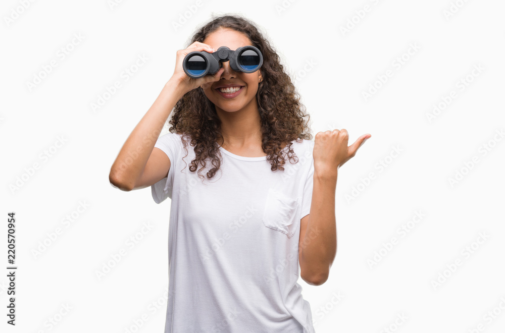 Young hispanic woman looking through binoculars pointing and showing with thumb up to the side with happy face smiling Young hispanic woman looking through binoculars pointing and showing with thumb up to the side with happy face smiling