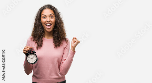 Young hispanic woman holding alarm clock screaming proud and celebrating victory and success very excited, cheering emotion © Krakenimages.com