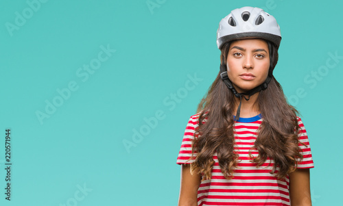 Young arab cyclist woman wearing safety helmet over isolated background with serious expression on face. Simple and natural looking at the camera.