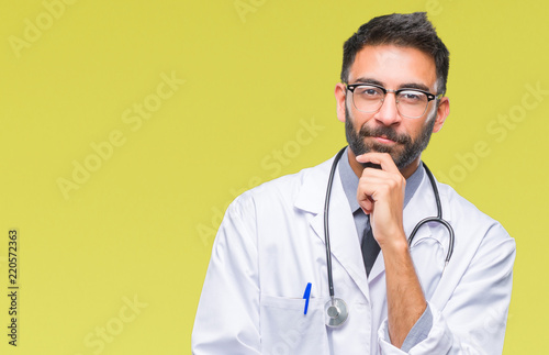 Adult hispanic doctor man over isolated background looking confident at the camera with smile with crossed arms and hand raised on chin. Thinking positive.