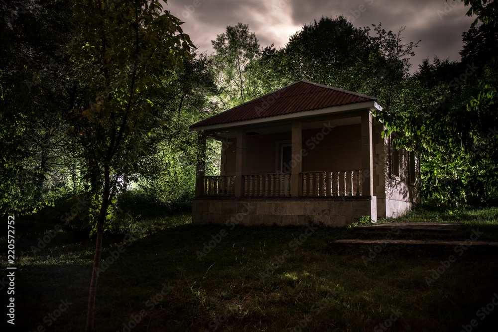 Mountain night landscape of building at forest at night with moon or vintage country house at night with clouds and stars. Summer night.