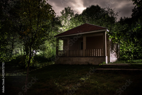 Mountain night landscape of building at forest at night with moon or vintage country house at night with clouds and stars. Summer night.