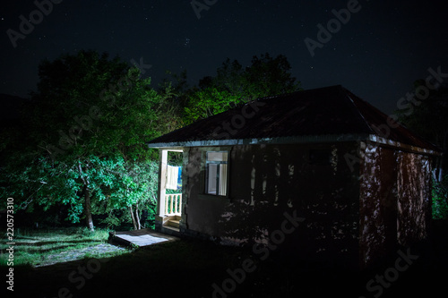 Mountain night landscape of building at forest at night with moon or vintage country house at night with clouds and stars. Summer night.