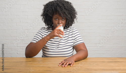 Young african american woman sitting on the table drinking a glass of milk with a confident expression on smart face thinking serious
