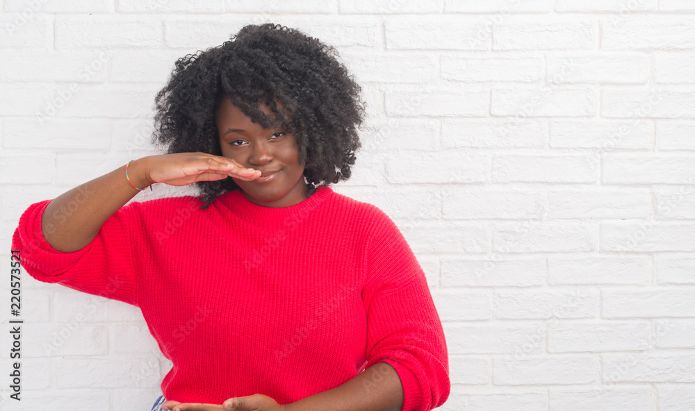Young african american plus size woman over white brick wall gesturing with hands showing big and large size sign, measure symbol. Smiling looking at the camera. Measuring concept. Young african american plus size woman over white brick wall gesturing with hands showing big and large size sign, measure symbol. Smiling looking at the camera. Measuring concept.