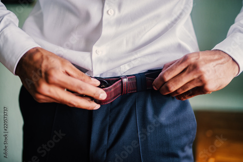 Close up of mans hands putting belt on his pants.