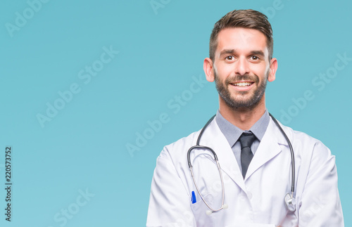 Young handsome doctor man over isolated background happy face smiling with crossed arms looking at the camera. Positive person.