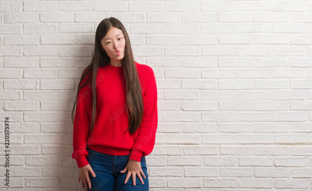 Young Chinese woman over brick wall making fish face with lips, crazy and comical gesture. Funny expression. Young Chinese woman over brick wall making fish face with lips, crazy and comical gesture. Funny expression.