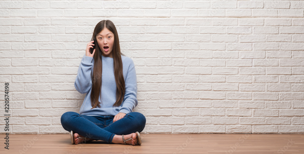 Young Chinese woman sitting on the floor over brick wall scared in shock with a surprise face, afraid and excited with fear expression Young Chinese woman sitting on the floor over brick wall scared in shock with a surprise face, afraid and excited with fear expression