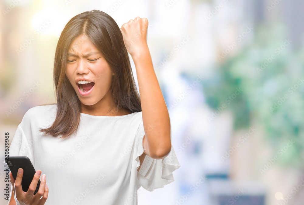 Young asian woman texting using smartphone over isolated background annoyed and frustrated shouting with anger, crazy and yelling with raised hand, anger concept