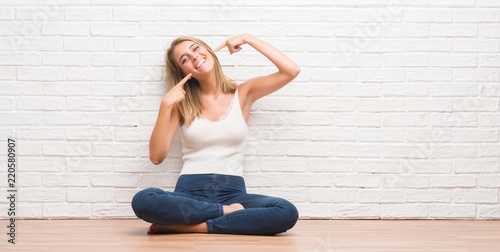 Beautiful young woman sitting on the floor at home smiling confident showing and pointing with fingers teeth and mouth. Health concept.