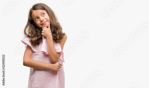 Brunette hispanic girl wearing pink dress looking confident at the camera with smile with crossed arms and hand raised on chin. Thinking positive. © Krakenimages.com