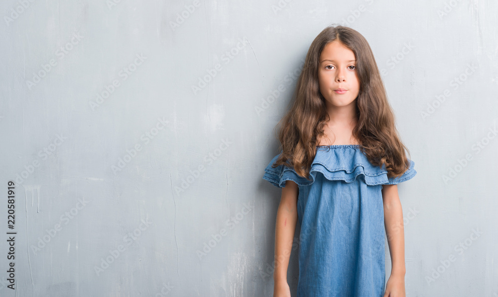 Fototapeta premium Young hispanic kid over grunge grey wall with serious expression on face. Simple and natural looking at the camera.