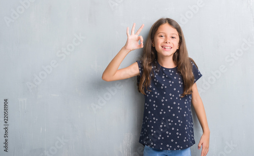 Young hispanic kid over grunge grey wall smiling positive doing ok sign with hand and fingers. Successful expression.