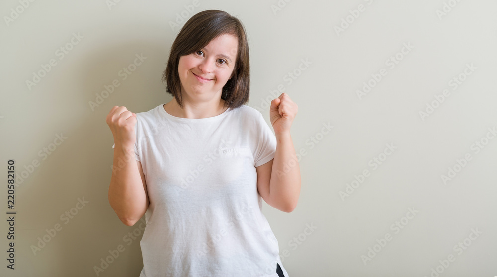Down syndrome woman standing over wall very happy and excited doing winner gesture with arms raised, smiling and screaming for success. Celebration concept. Down syndrome woman standing over wall very happy and excited doing winner gesture with arms raised, smiling and screaming for success. Celebration concept.