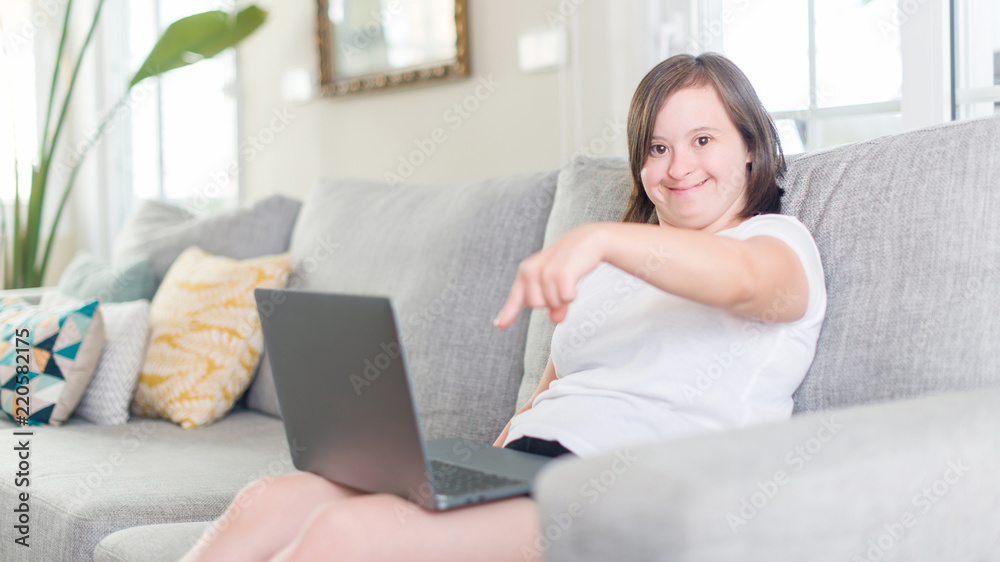 Down syndrome woman at home using computer laptop very happy pointing with hand and finger Down syndrome woman at home using computer laptop very happy pointing with hand and finger