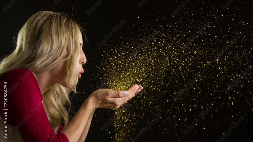 Pretty woman blowing glitter at the camera.