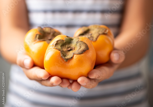 Hand holding persimmon fruit for giving photo
