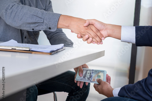 Hands passing money under table corruption bribery, businessman sealing the deal with a handshake and receiving a bribe money.